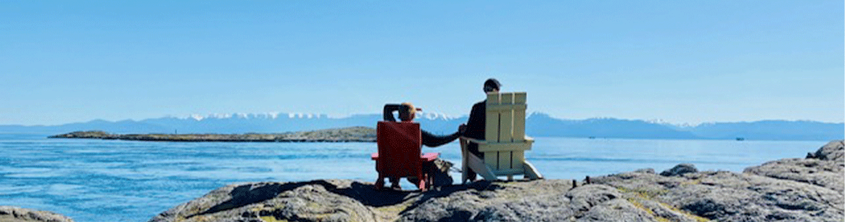 Couple-looking-at-ocean Couple sitting in red and yellow Muskoka chairs facing ocean
