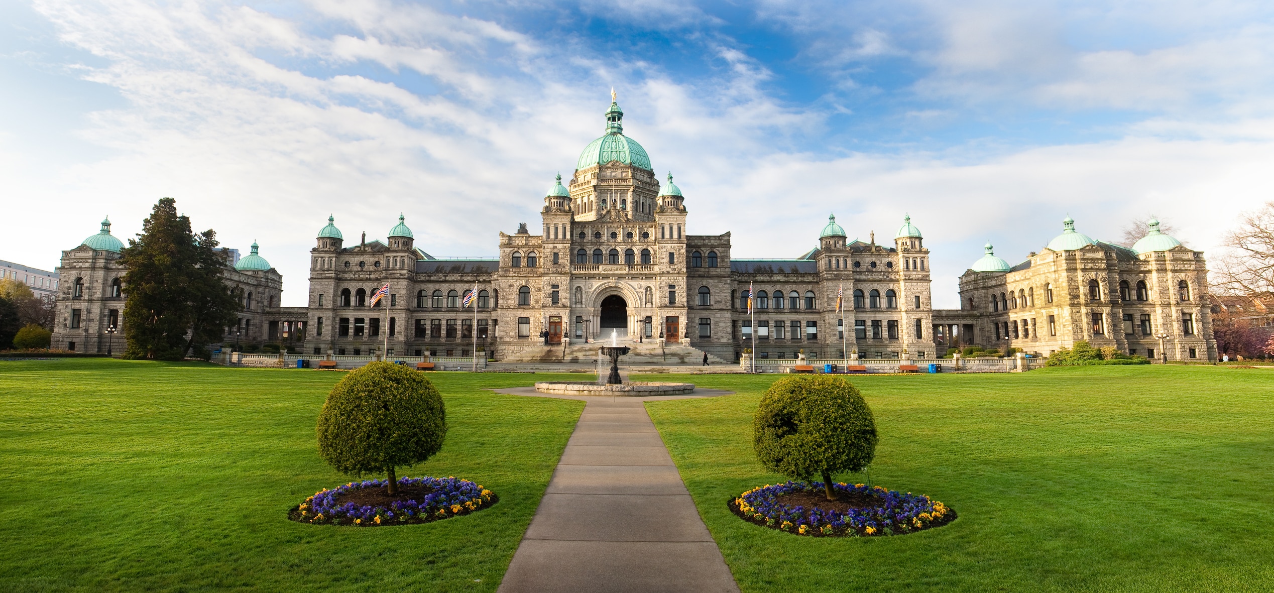 Frontal view of BC Parliament Buildings with bright green lawn and blue sky